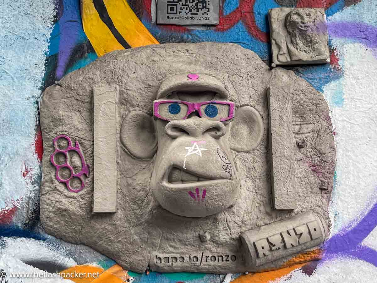 concrete wall sculpture of a face wearing pink spectacles and a cap