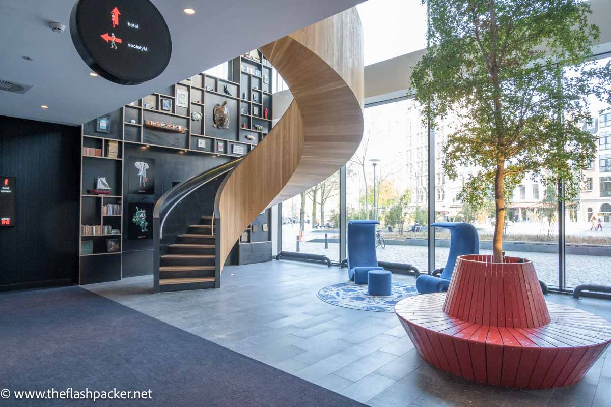 entrance lobby of hotel with wooden spiral stair andsmall tree in red holder