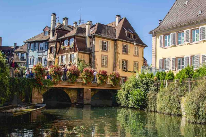 pastel coloured houses and a stone bridge with flowers by a canal in colmaw