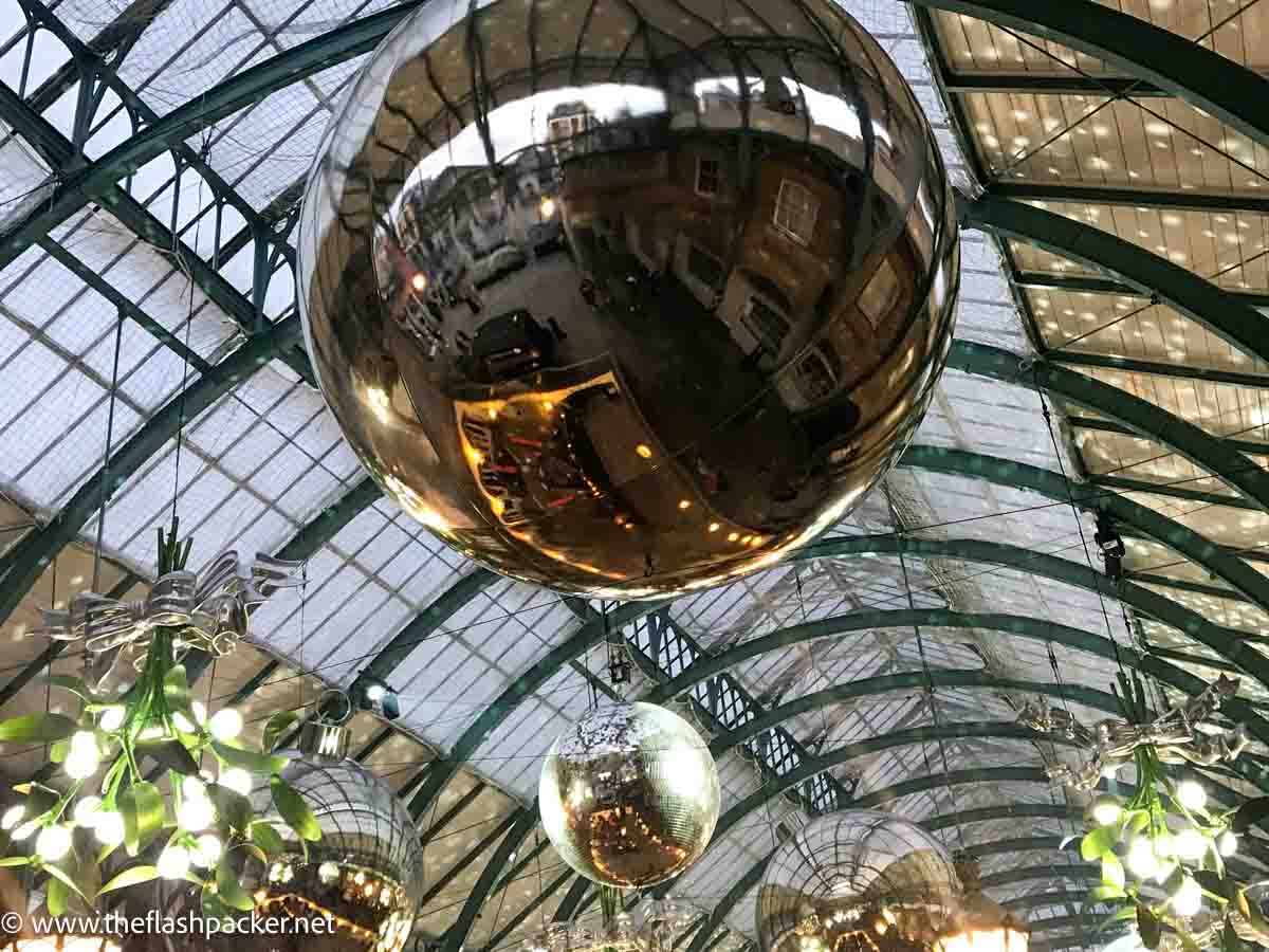 giant bauble hanging from iron and glass roog reflecting buildings of covent garden