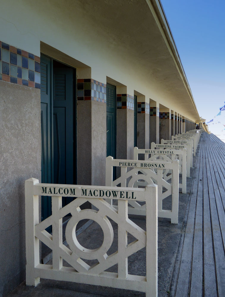 row of beach houses on wooden walkway each with name of someone in film industry in deauville normandy