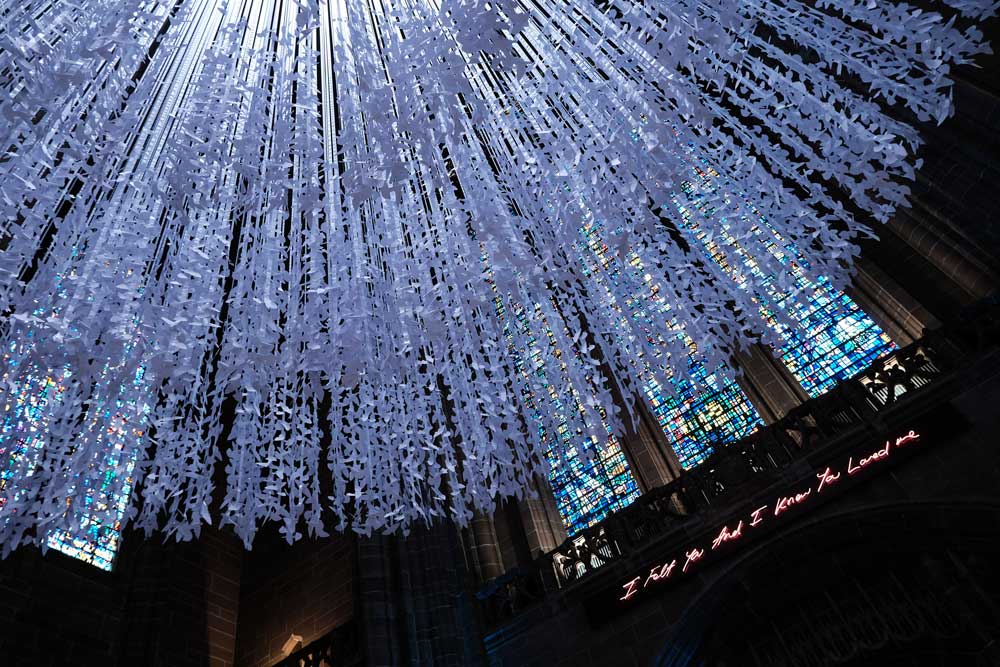 art installation of doves made of white paper in front of stained glass window