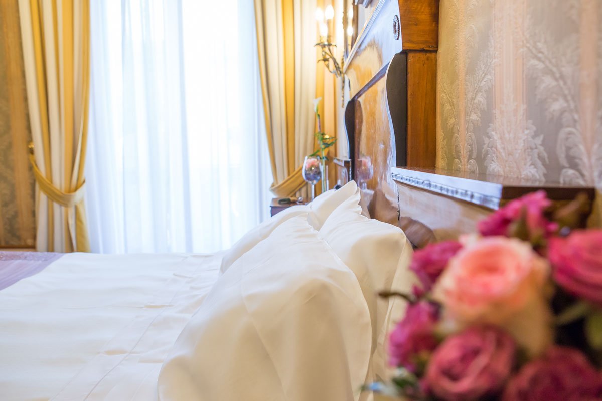 a verona 5 star hotel bedroom with bed behind a vase of pink and red roses