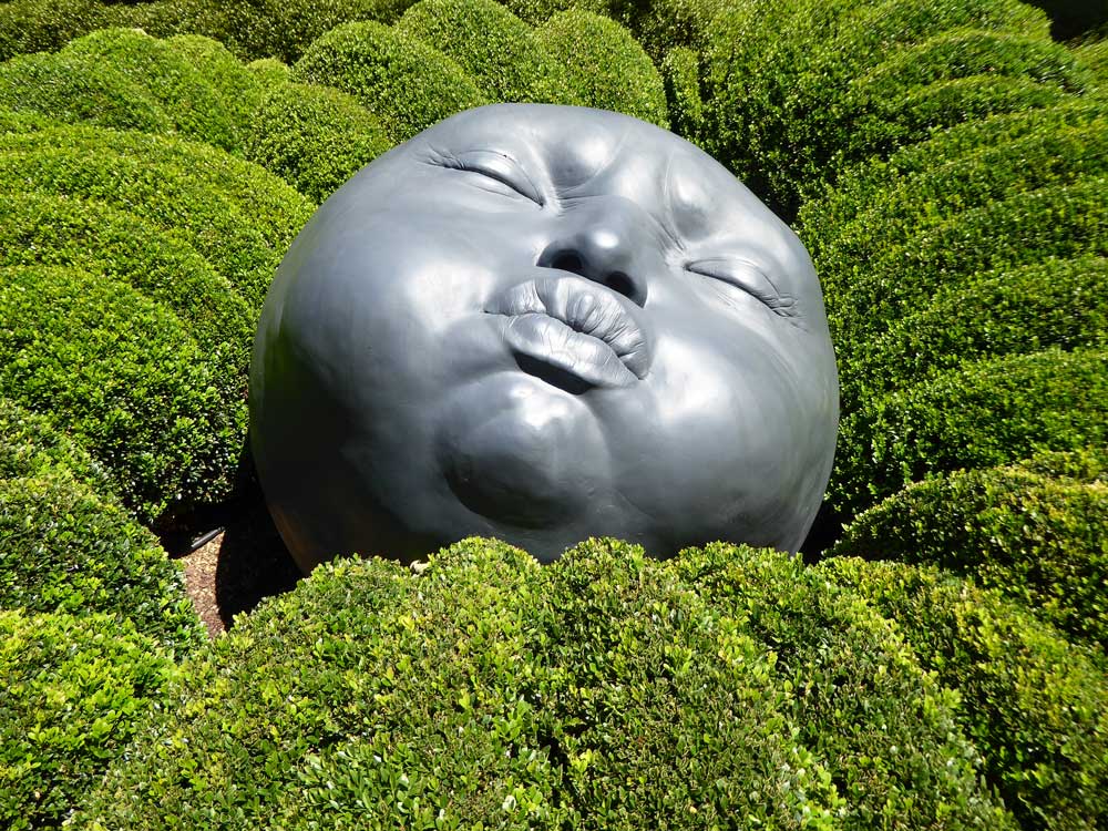 sculpture of child's head ion bushes of garden in etretat france