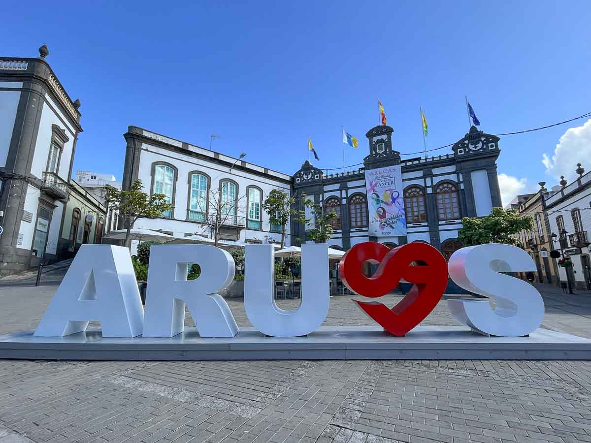 sign spelling arucas in a square in front of 2-storey grey and white buildings