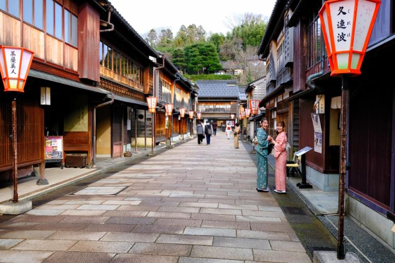 two women in kimonos posing in a street lined with traditional buildings in kanazawa japan