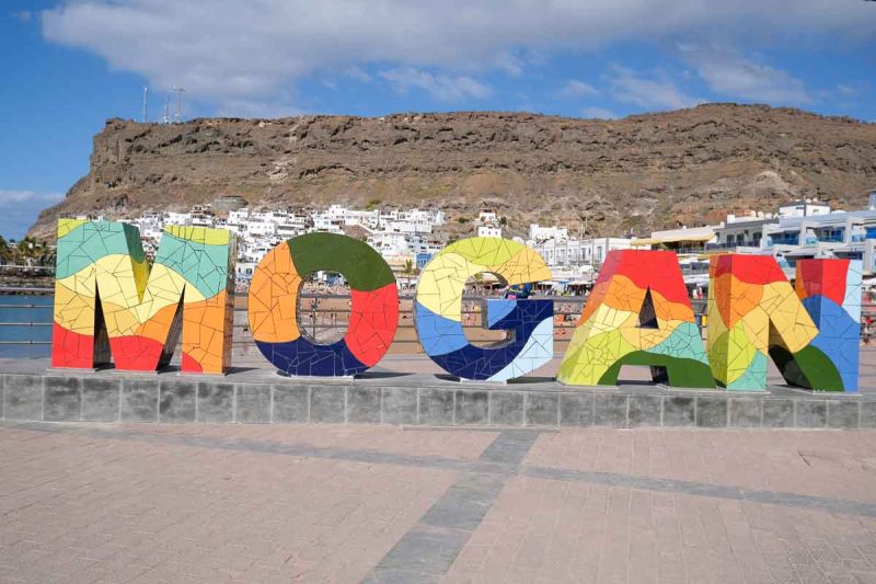 multicoloured sign spelling mogan in front of a beach and cliff face