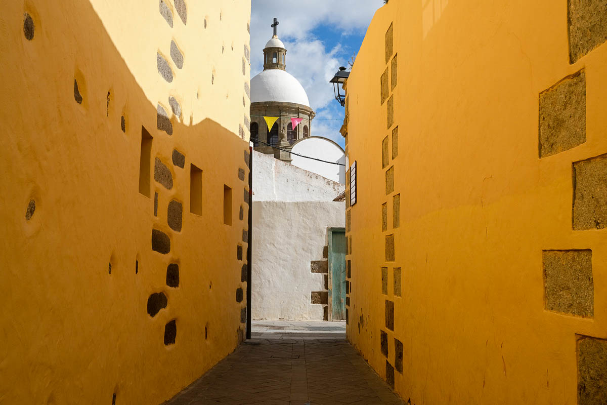 narrow alleyway with yellow walls with view of dome of church in aguimes gran canaria