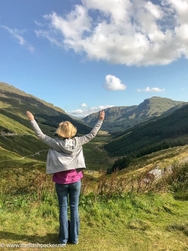 woman standing with arms outstretched overlooking valley