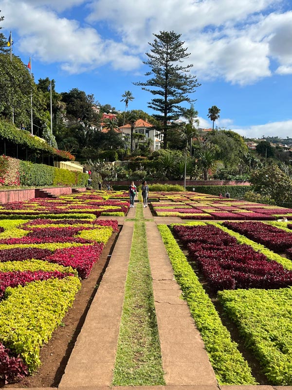 2 people walking on path in a formal garden laid out with geometric patterns of purple and green foliage