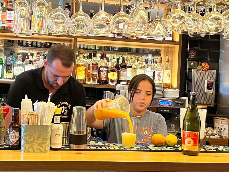 mand and woman behind a bar pouring poncha drink into a glass from a jug