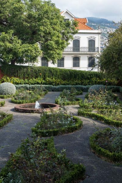 small paved garden with fountain in front of large whitewashed villa