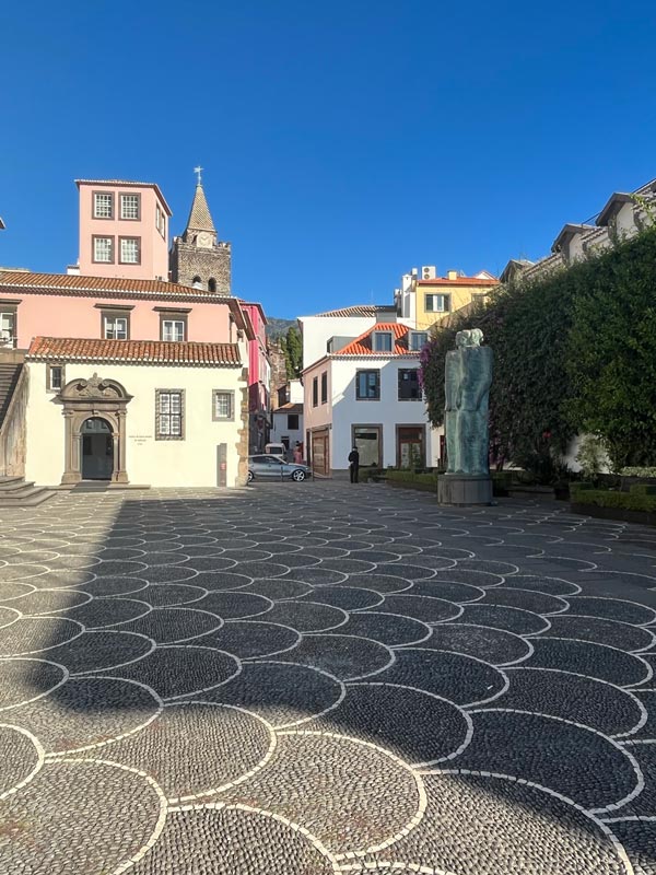 attractive square with seashell patterned mosaic pavement and small white chapel in front of pink building