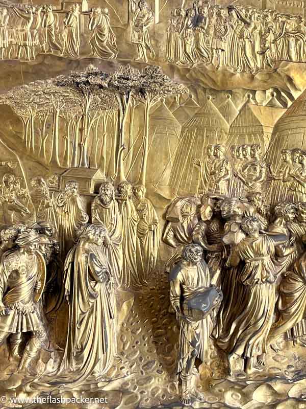 bas relief in bronze of a group of people with trees and tents