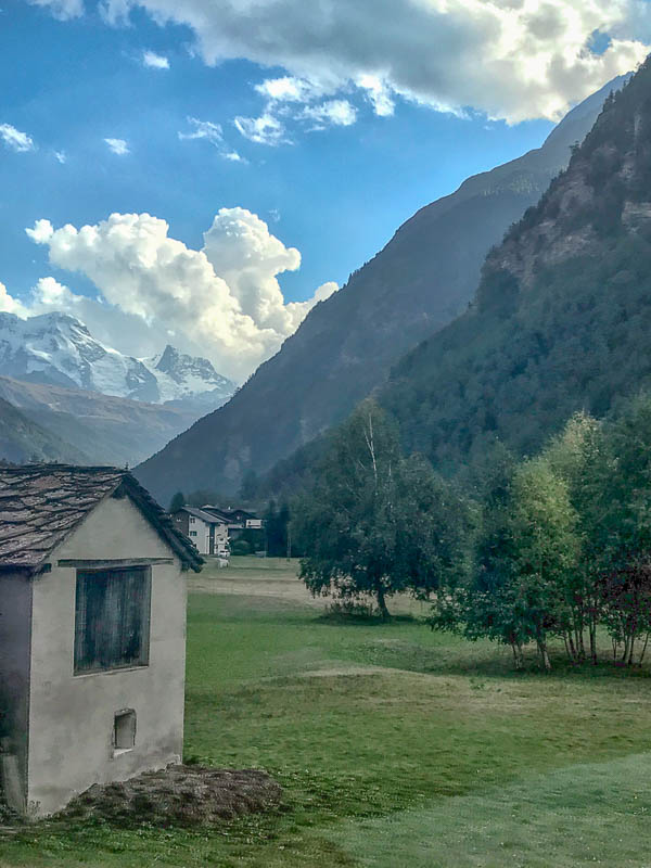 a small pasture in switzerland with the backdrop of snow capped mountains