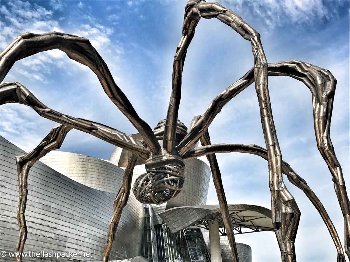 sculptre of a giant spider outside a metal plated modern building