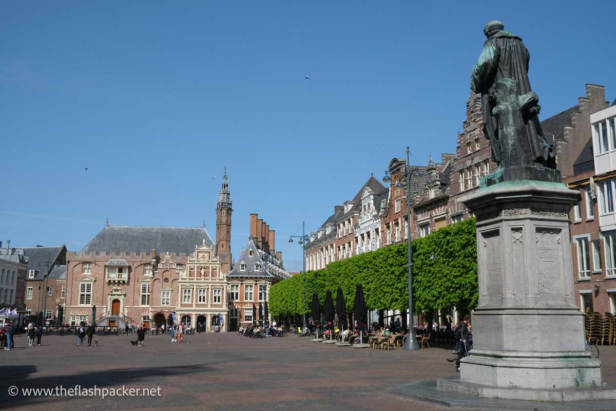 a large square in haarlem with a big statue , medieval buildings and cafe tables