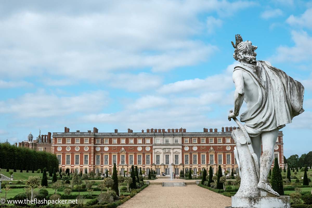 arge statue overlooking wide red brick exterior of hampton court palace