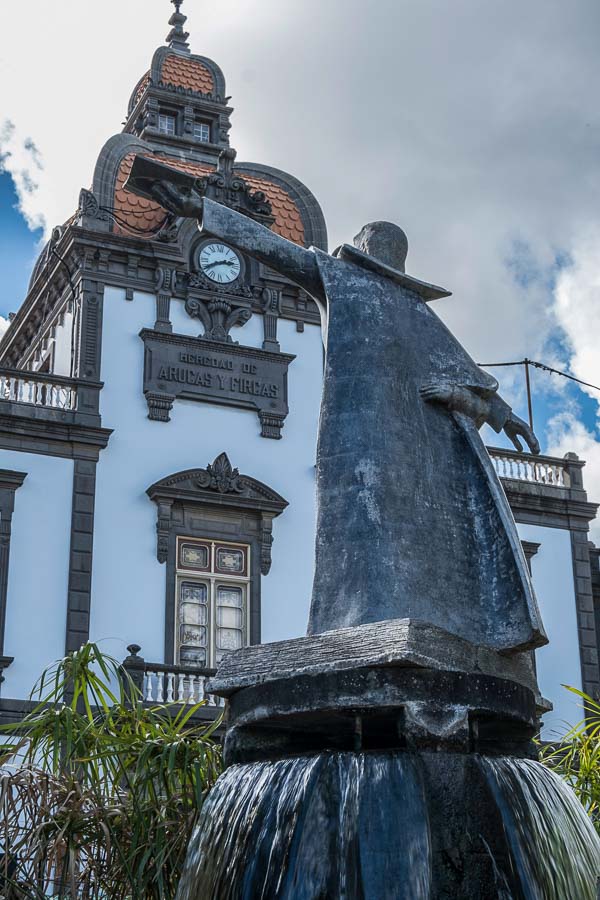 large bronze statue of a person holding out a book in front of an art nouveau building