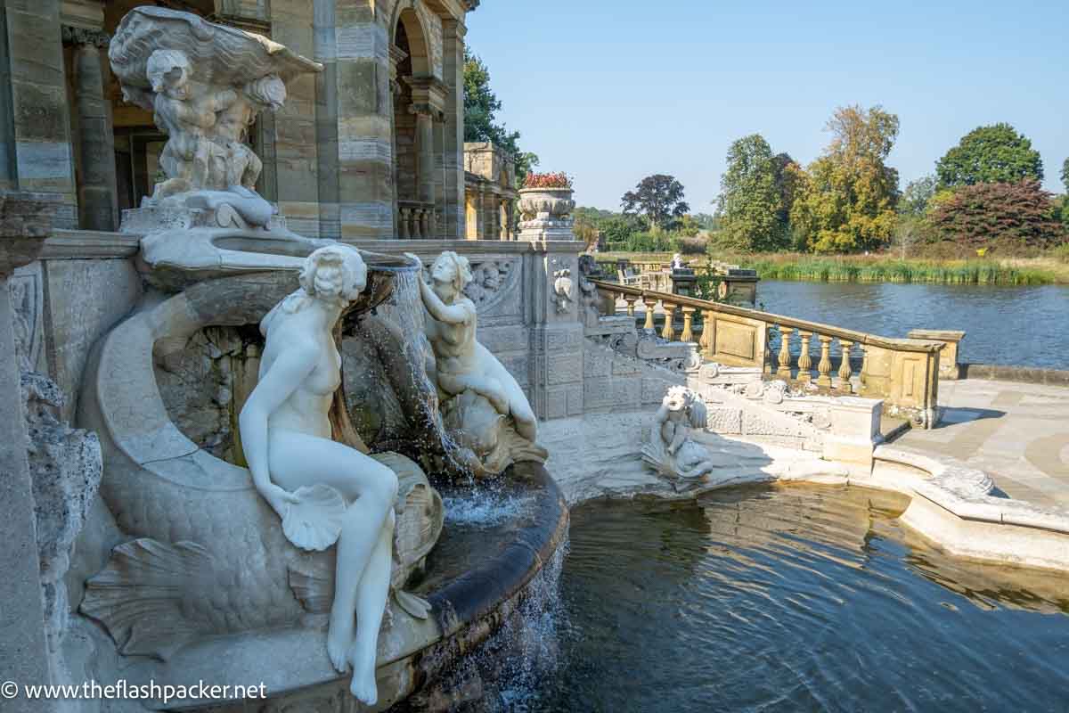 large fountain with 2 naked female figures next to a lake