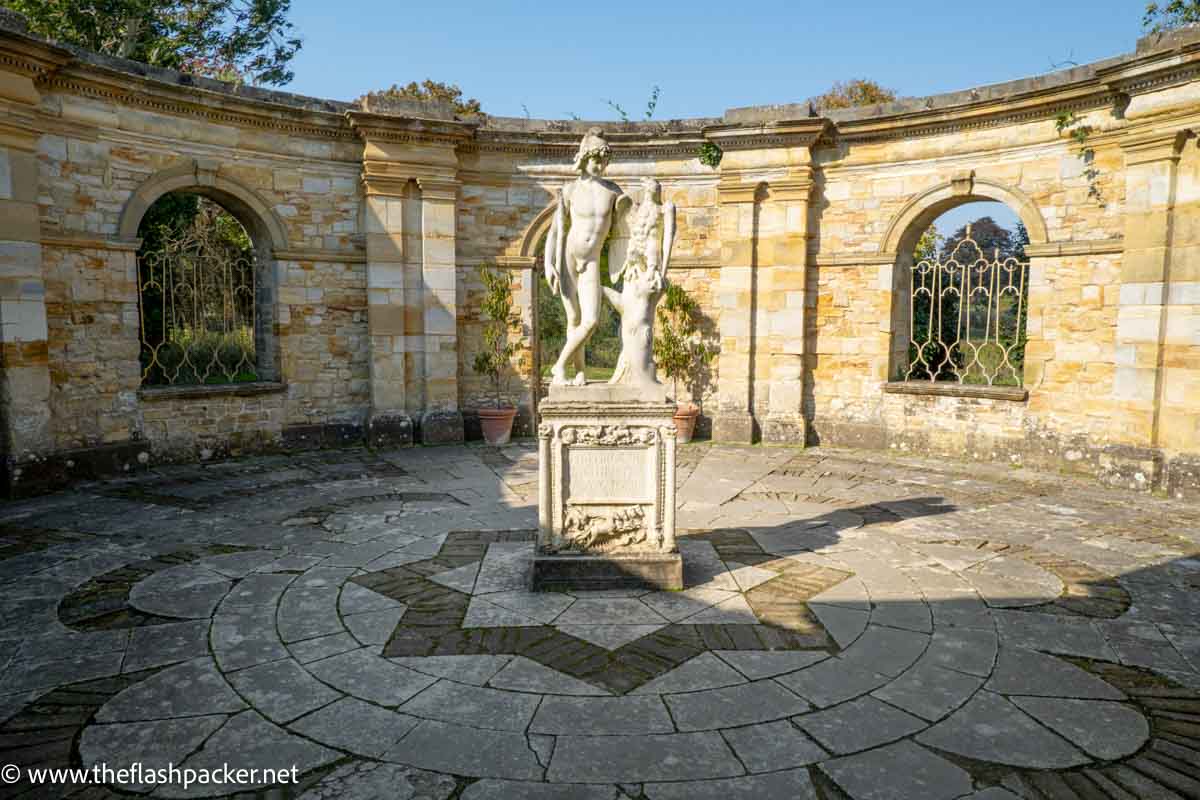 state of naked young male in the centre of a walled garden courtyard