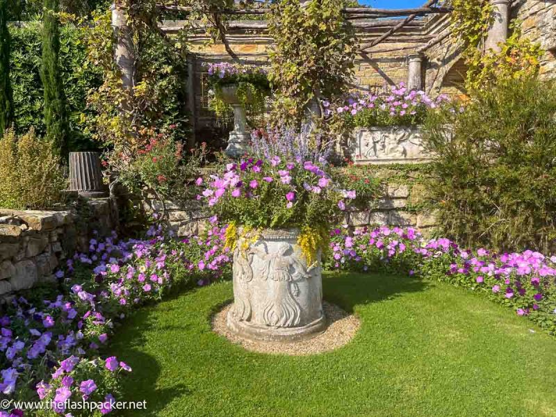 decorated urn planted and surrounded by pink and purple flowers