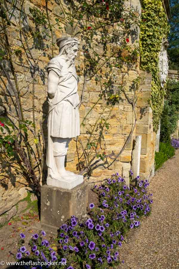 classical stone statue of bearded figure next to a garden wall