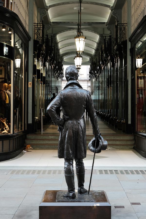 bronze sculpture of gentleman in front of arcade of shops in london