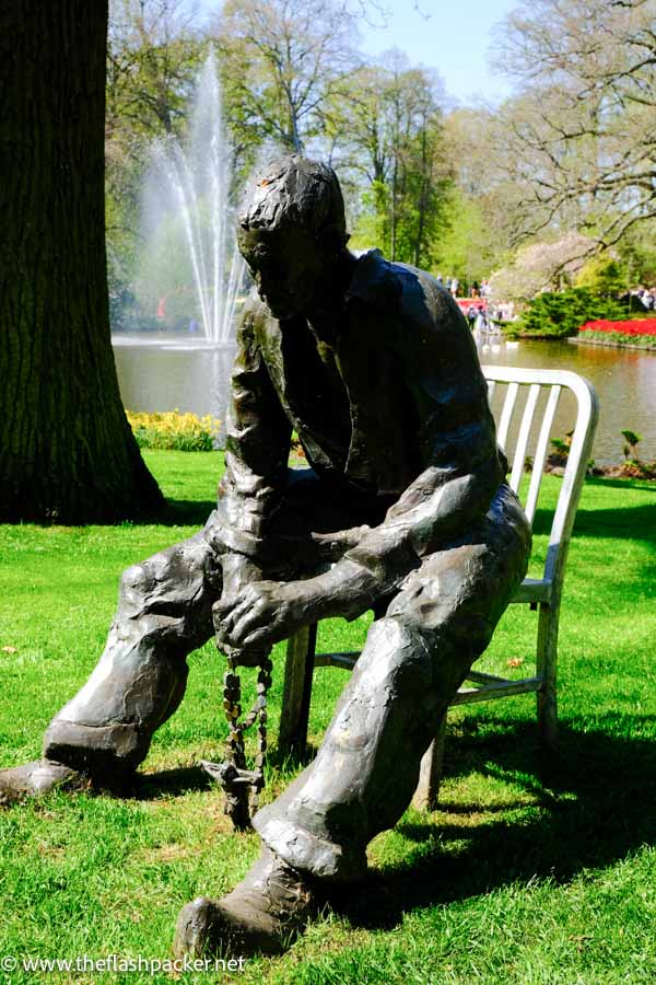 bronze sculpture of man sitting on chair with rosary