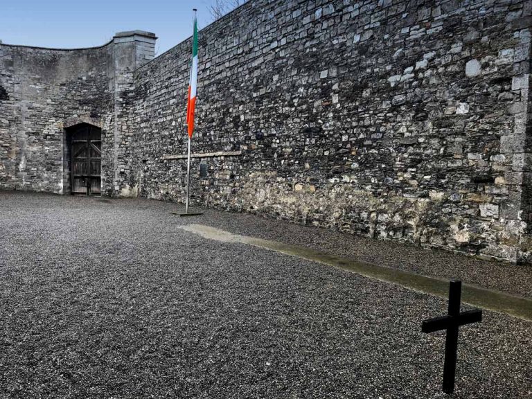 courtyard with stone walls and cross and tricolor flag at kilmainham gaol dublin