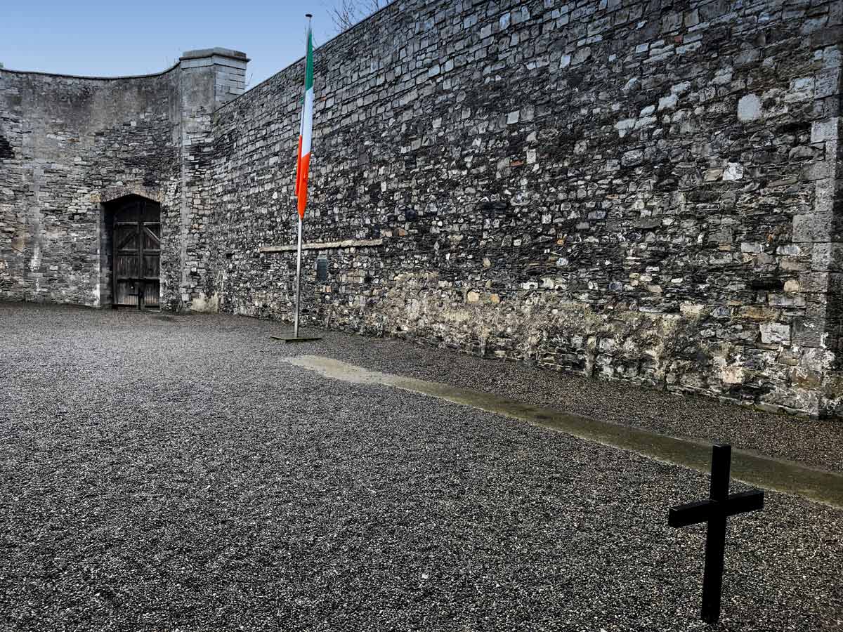 courtyard with stone walls and cross and tricolor flag seen when visiting kilmainham gaol dublin