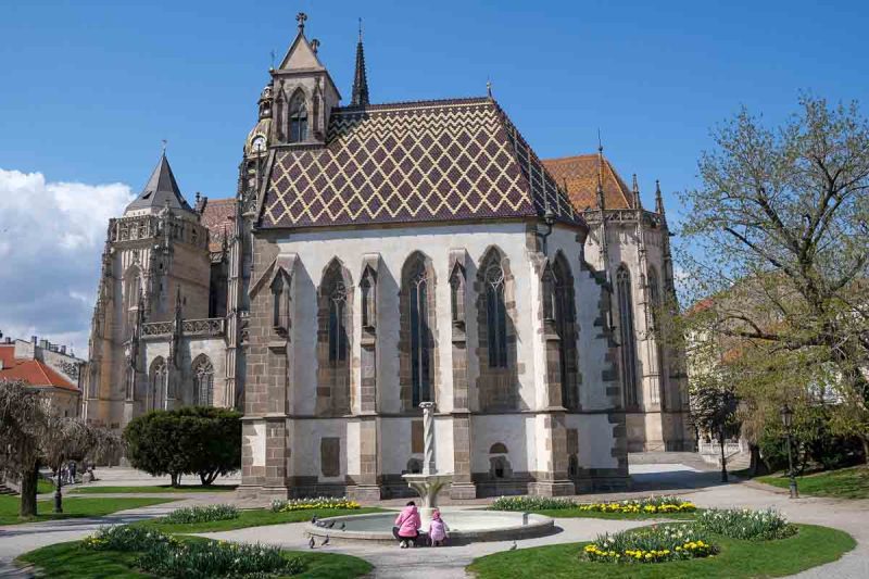 women and child kneeling down by fountain in front of st michaels curch in kosice