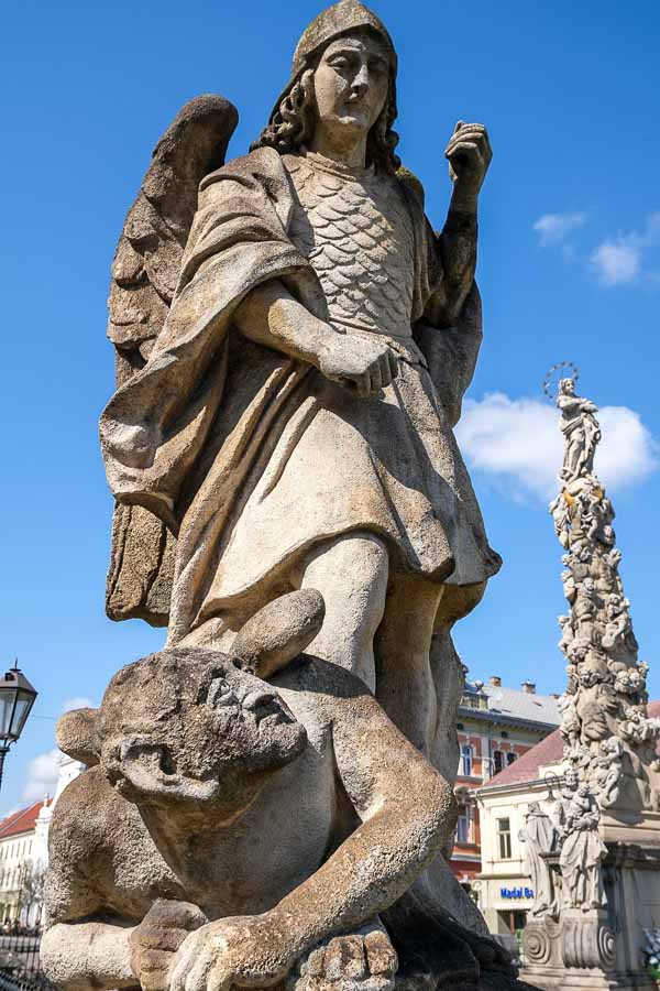 gnarled gothic stone sculpture of a devil under the foot of an angel