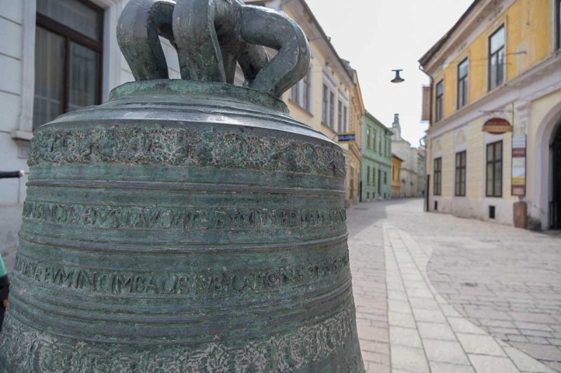 large bronze bell sitting at the top of an empty street in kosice slovakia