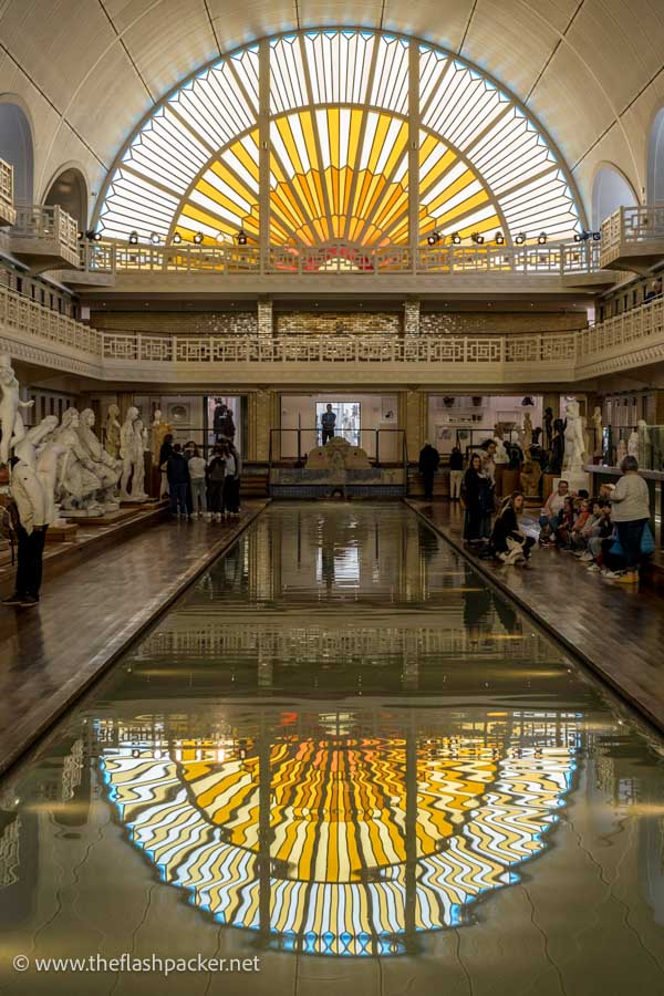 half-moon-shaped stained glass window reflected in the shallow water of an old swimming pool