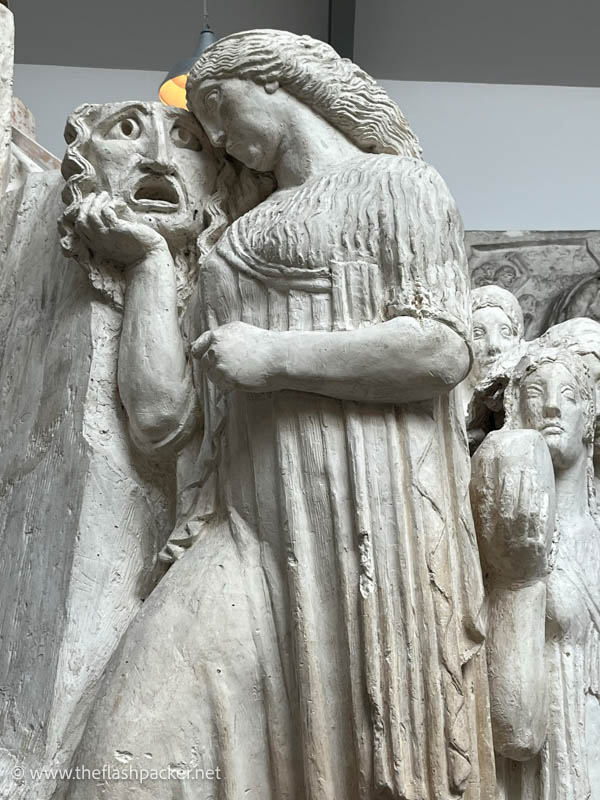 stone sculpture of a woman holding a mask