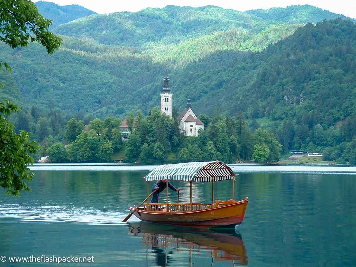 man rowing boat across lake with church in background