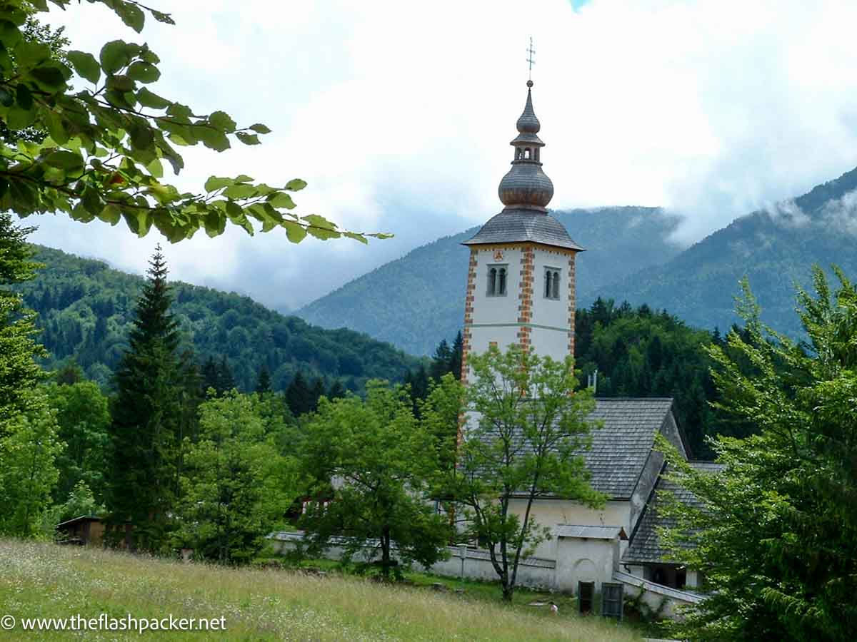 church with a spire in lush greenery against misty mountains