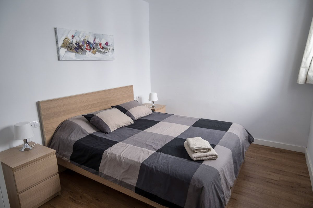 bedroom in a rental apartment with wooden floor and a bed with grey and beige checked linen