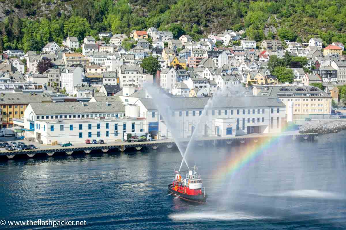 boat in pretty harbour of alesund with rainbow colours in water spray