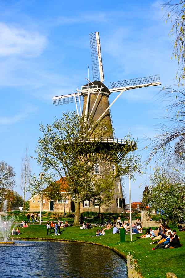 windmill at the side of canal with people sitting on canal bank