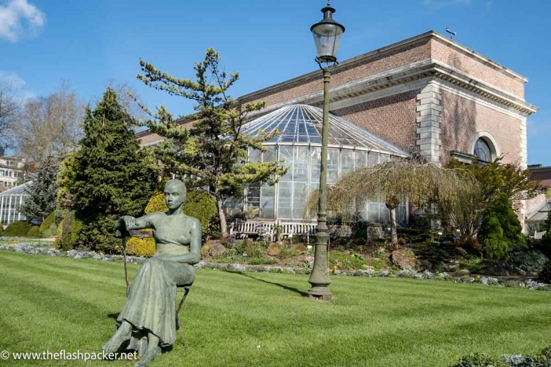 sculpture of a women sitting on a chair in front of a greenhouse