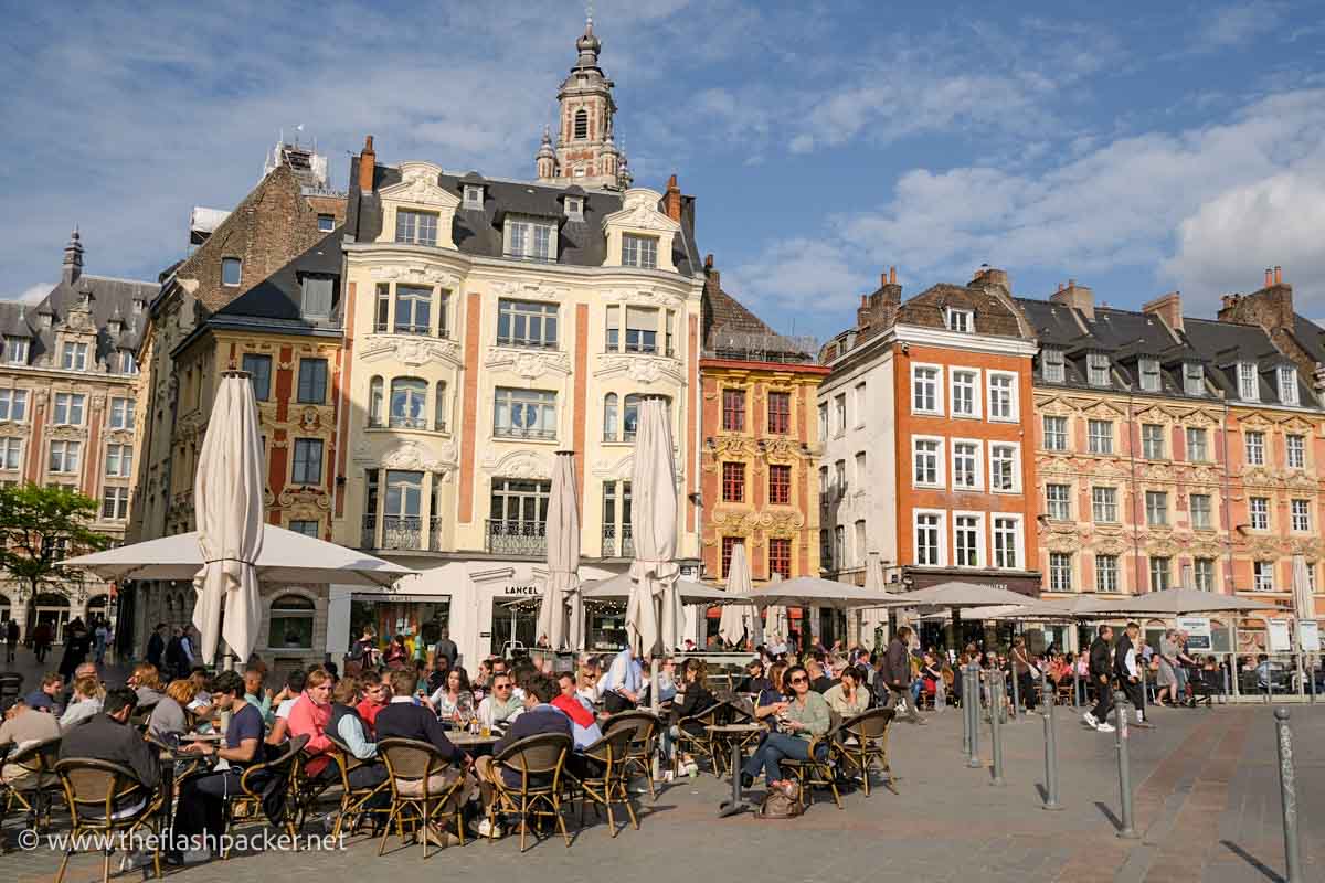 people sitting at outdoor cafe tables in a square lined with old buildings