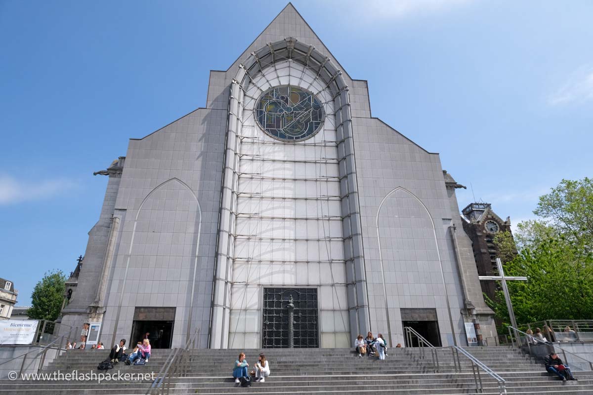 people sitting on steps outside the grey and white facade of lille cathedral