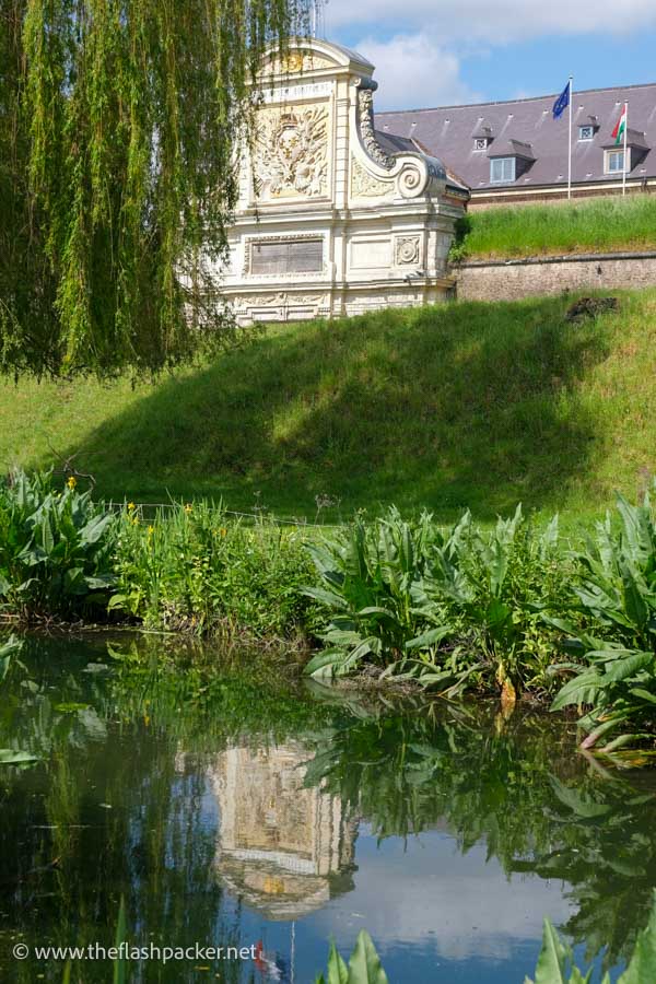 ornate facade of lille citadel reflected in whater next to a grassy bank