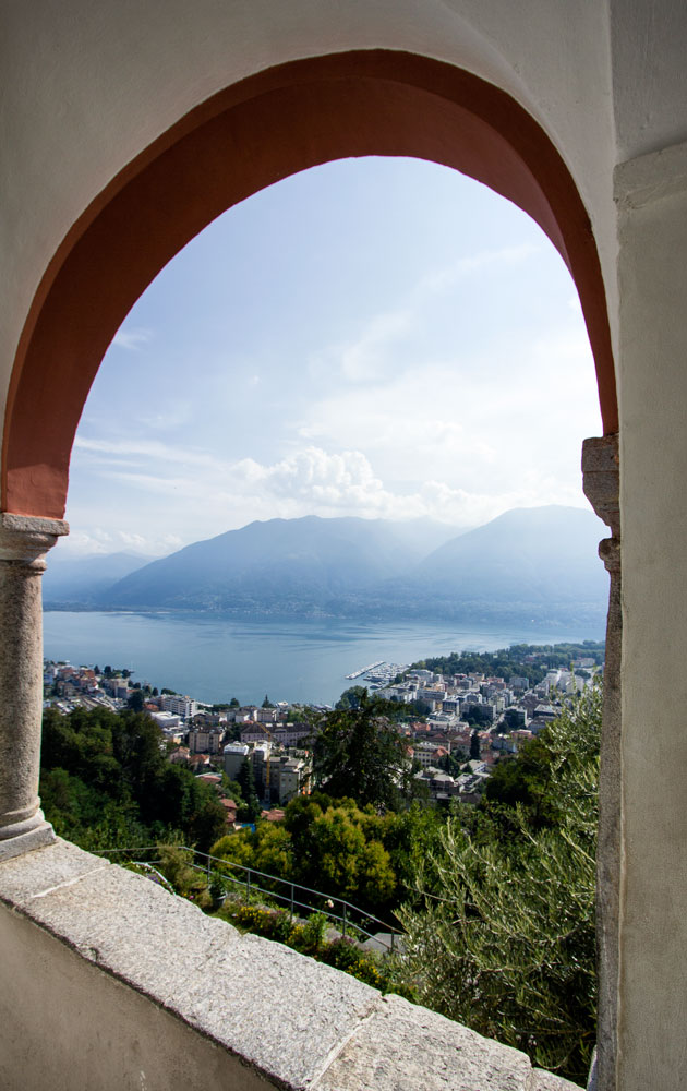 view of lake and mountains through the arched window of a church loggia