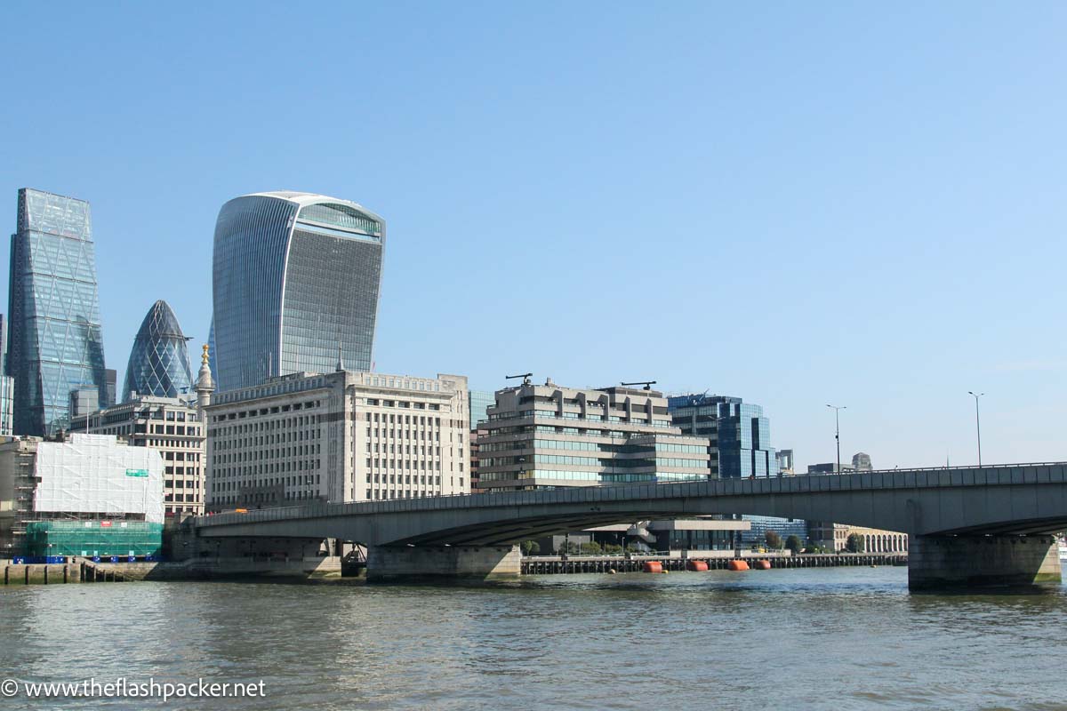 concrete london bridge over river thames with modern skyscrapers on bank