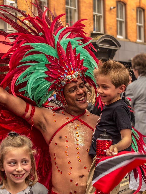 man wearing feathers for london pride carrying small child