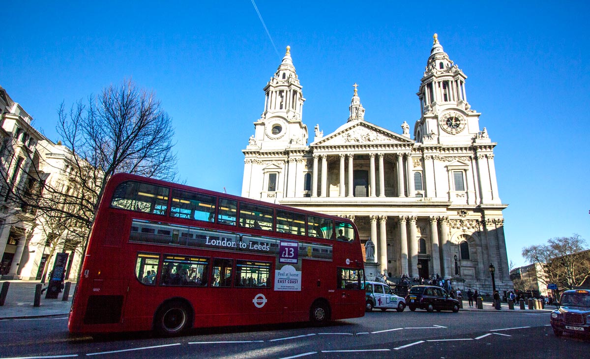 red double decker bus passing in front of a white neoclassical church