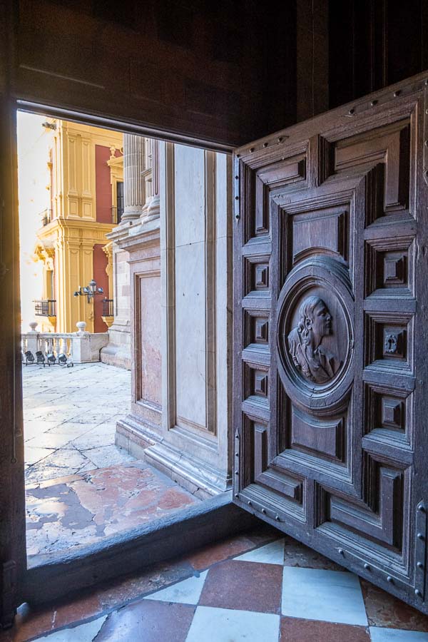 carved wooden door of malaga cathedral opening to sunny patio